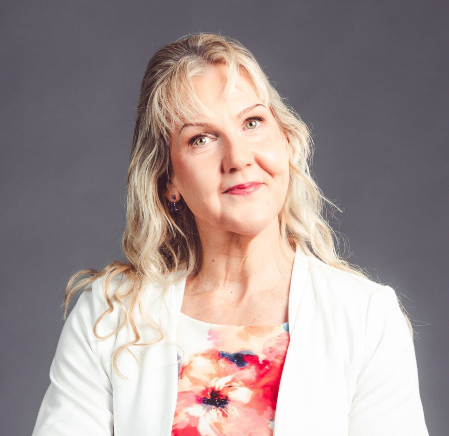 Pia Pohjola hymyilee, yllään valkoinen jakku ja kukkakuvioinen paita