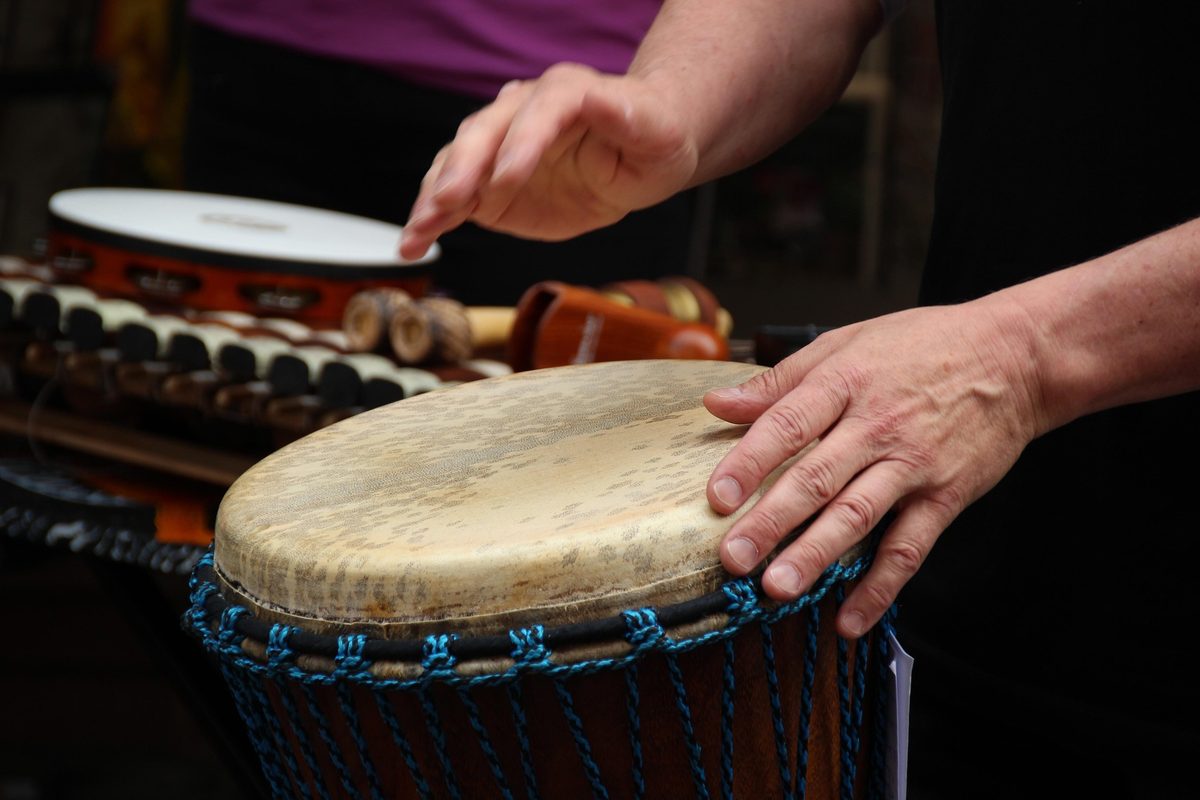 Kädet soittavat djembe-rumpua, taustalla muita lyömäsoittimia